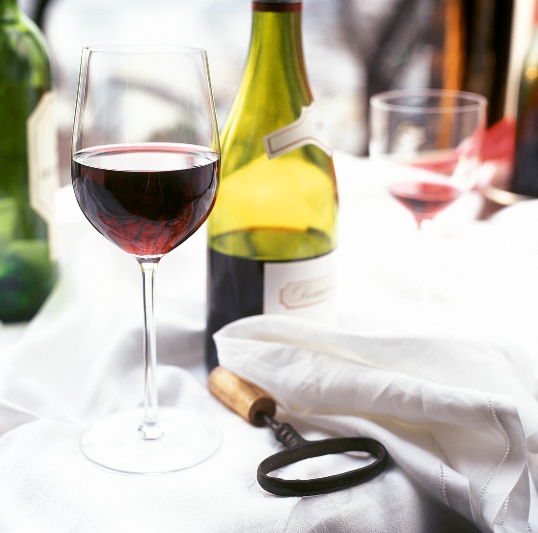 Glass of red wine on tablecloth, corkscrew, red wine bottle