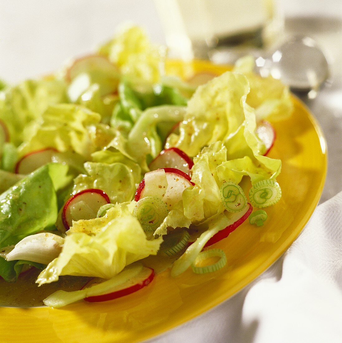Lettuce with mustard vinaigrette, radishes on a yellow plate