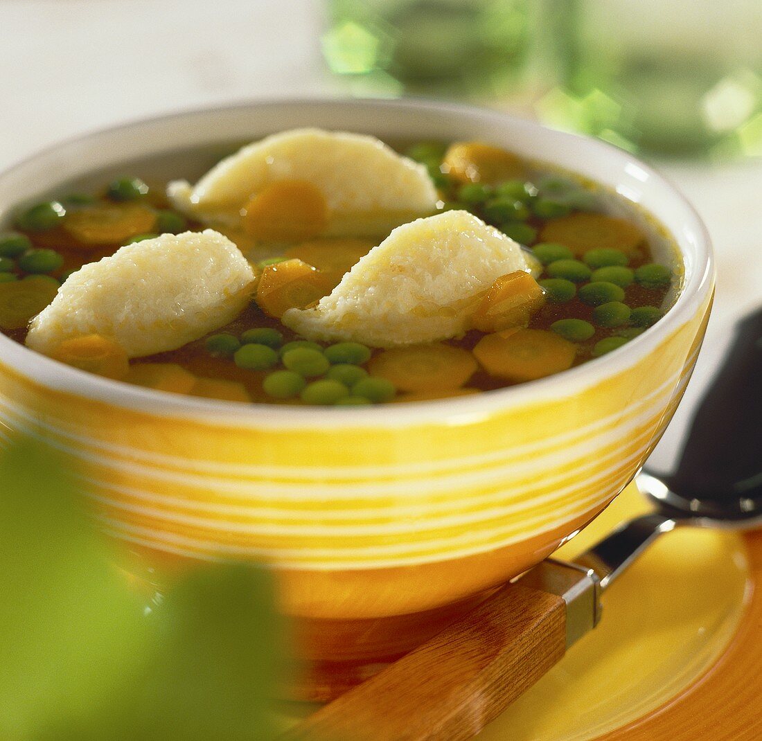 Clear vegetable soup with dumplings in yellow bowl