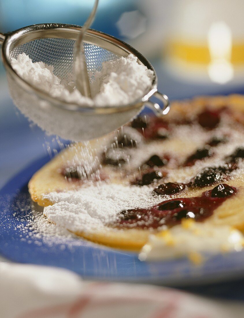 A blueberry pancake being sprinkled with icing sugar