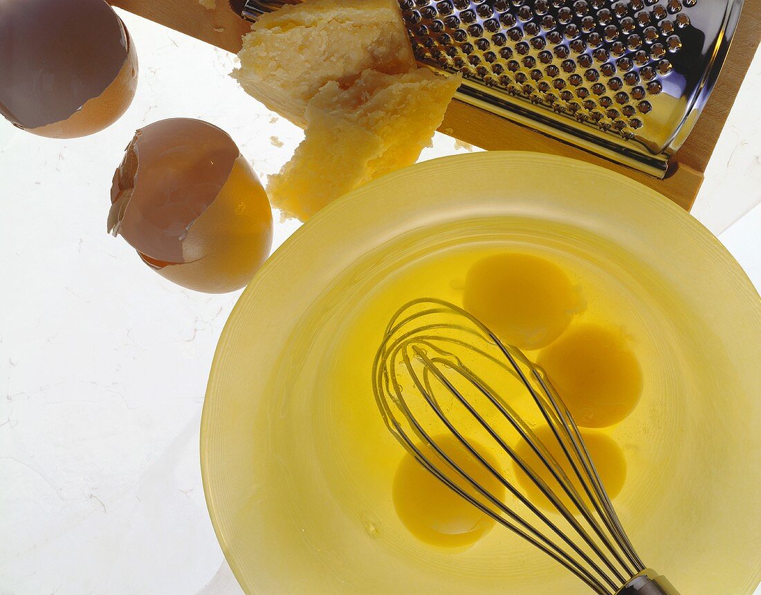 Aufgeschlagene rohe Eier, Eierschalen und Parmesan mit Reibe