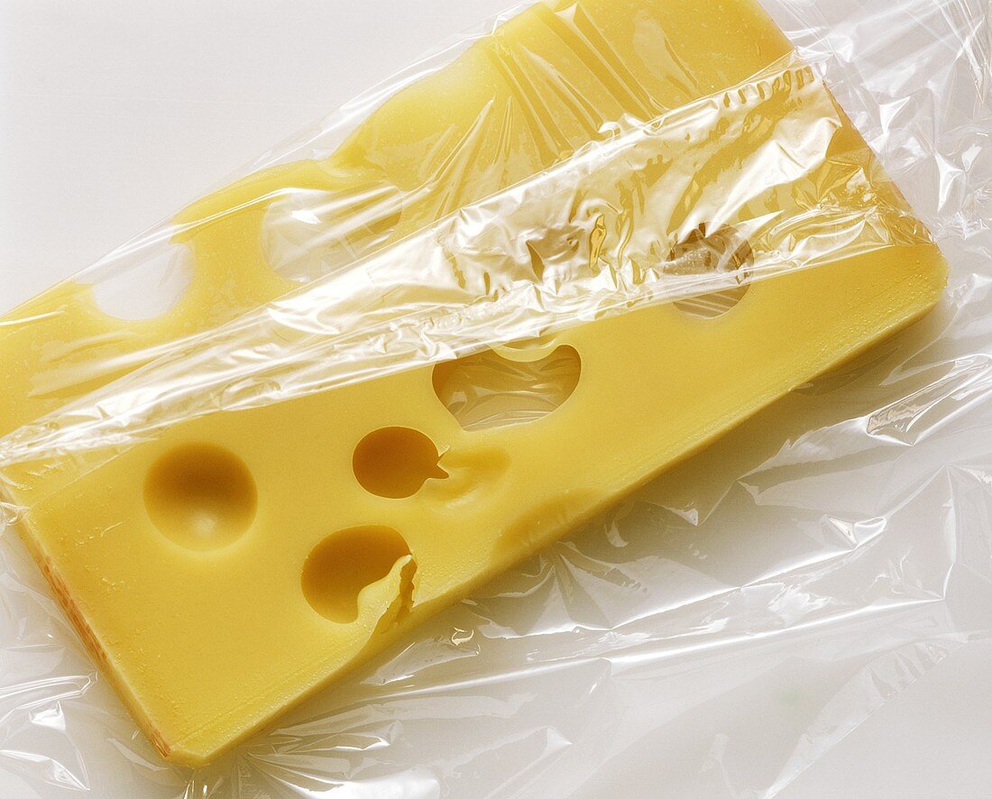 A piece of Emmental, half packed in transparent film