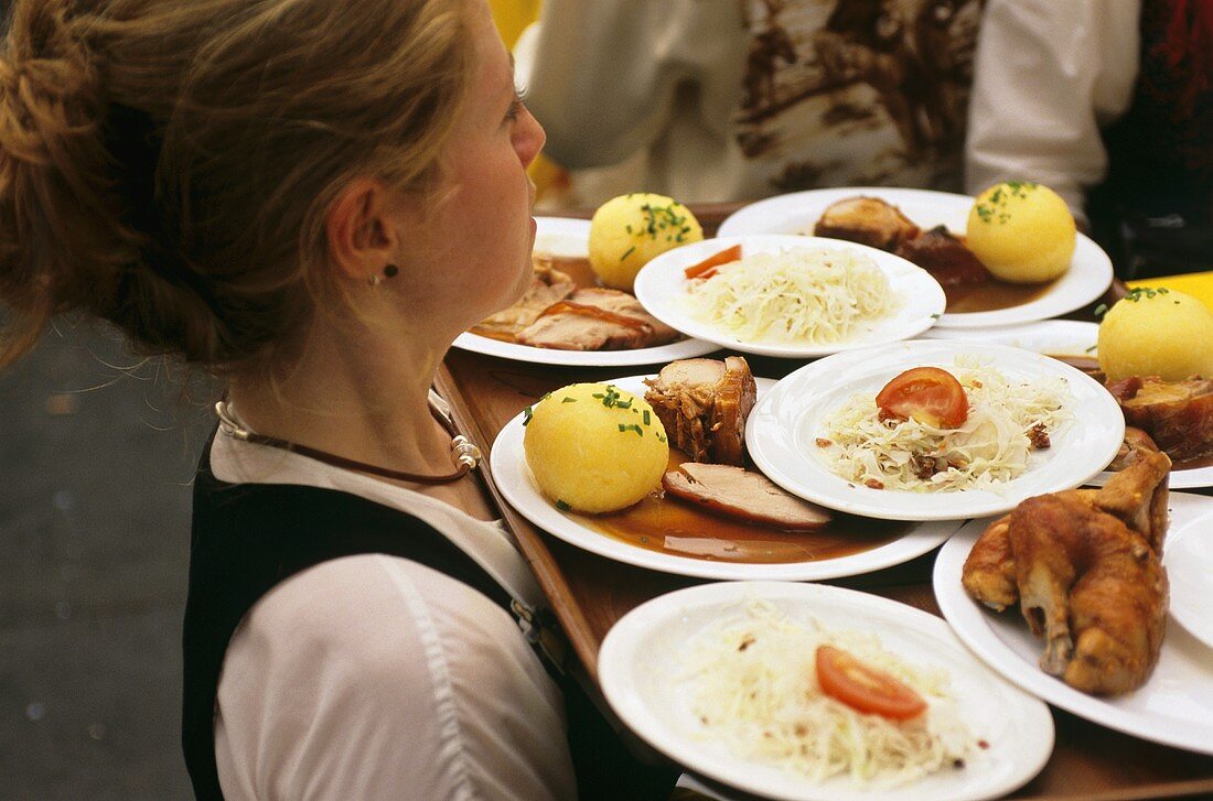 Kellnerin trägt Tablett mit vielen Gerichten am Oktoberfest