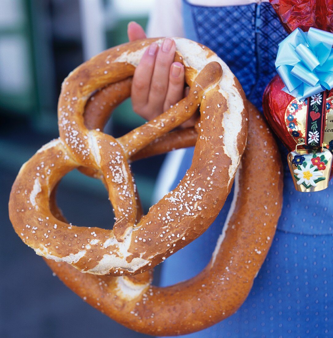 Woman in blue German costume holding two large pretzels