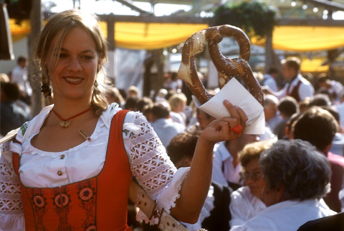 Junge Frau mit Riesenbrezel in der Hand am Oktoberfest
