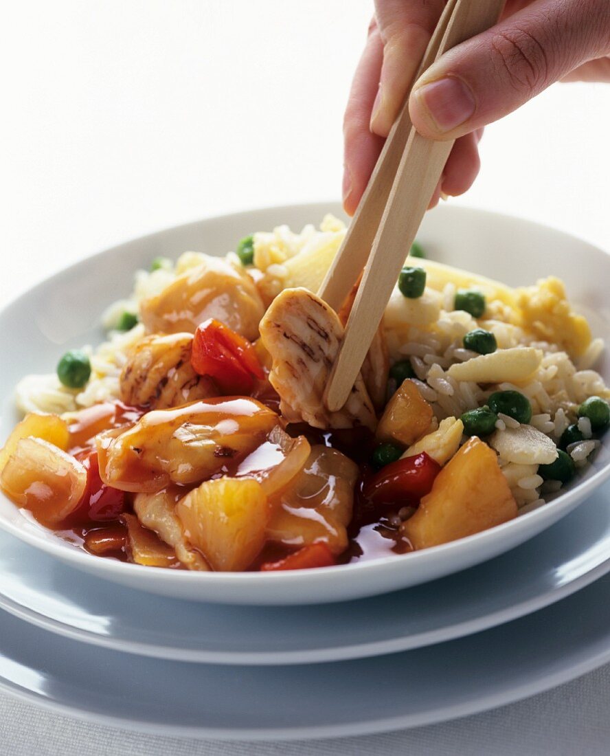Sweet & sour chicken with rice on plate; hand with chopsticks