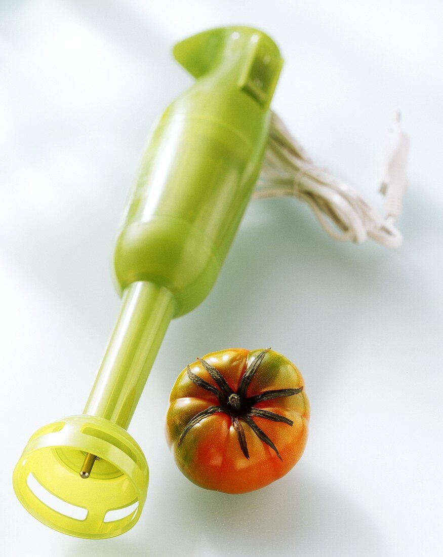Grüner elektrischer Pürierstab und eine Tomate
