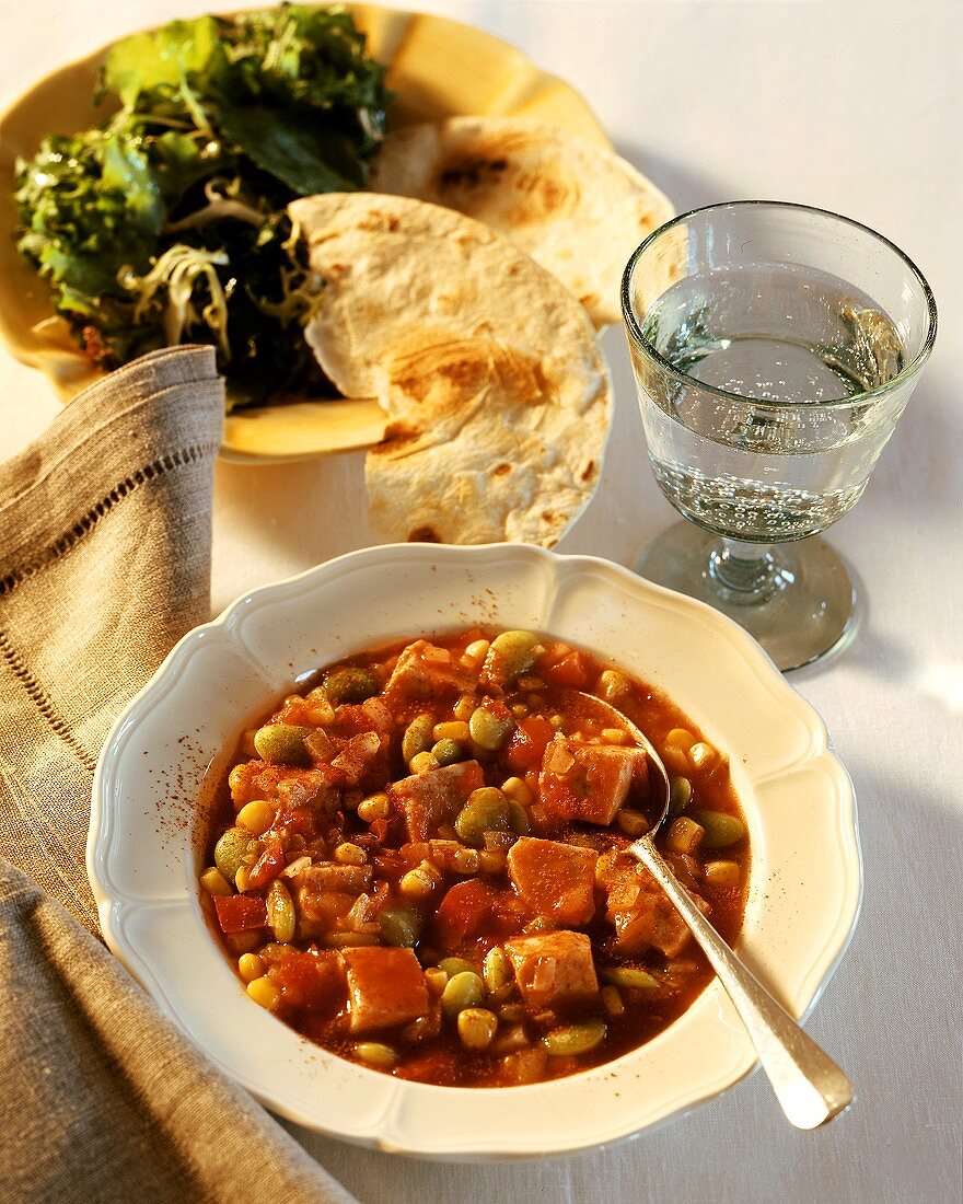Turkey and bean stew on plates; Mineral water; Bread; Salad