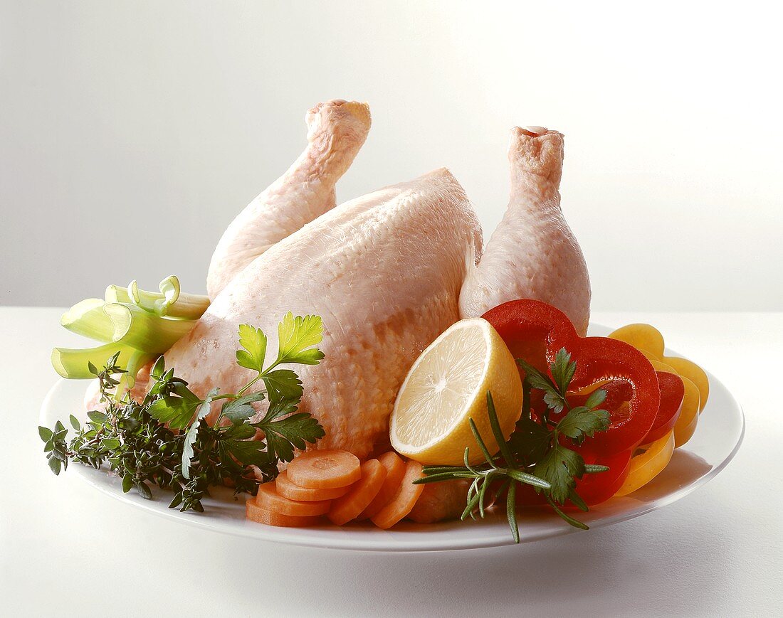 Rohes Huhn auf Teller mit Gemüse, Kräutern und Zitrone