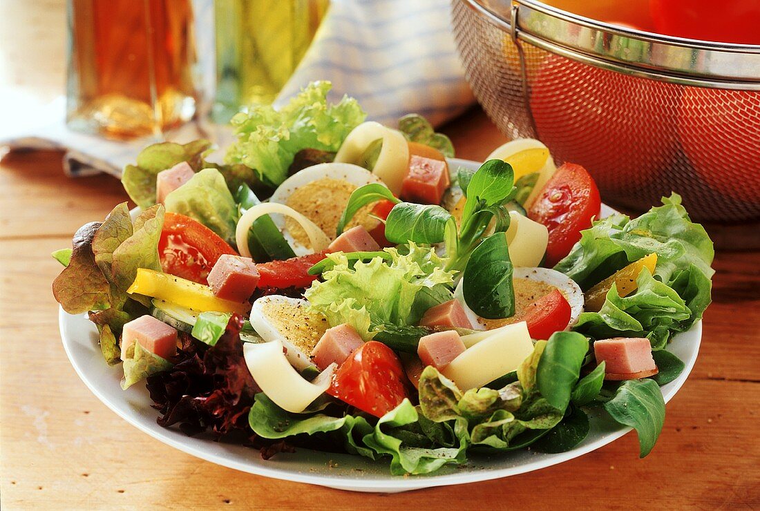 Green salad with ham on plate; oil and vinegar; tomatoes
