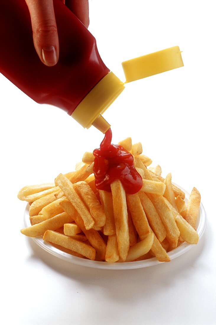 Pommes frites auf Teller mit Ketchup begiessen