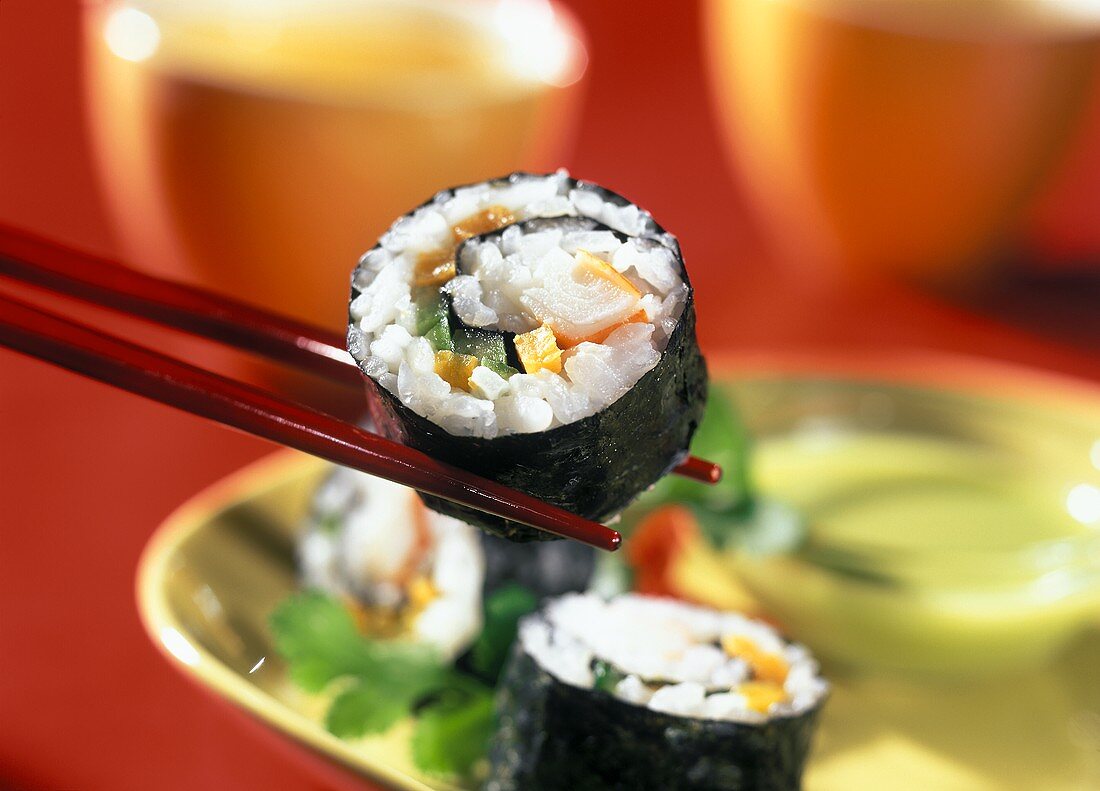 Maki sushi on chopsticks over a plate
