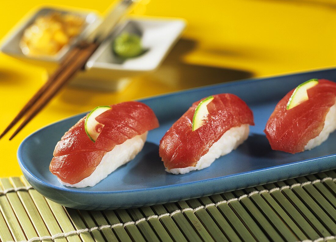 Nigiri-Sushi, verziert mit Gurkenschnitzen, auf blauem Teller