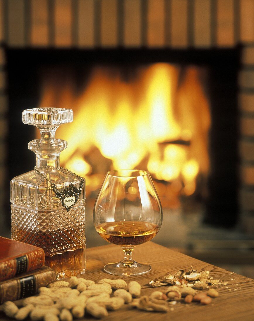 Brandy in glass and carafe on table in front of fire