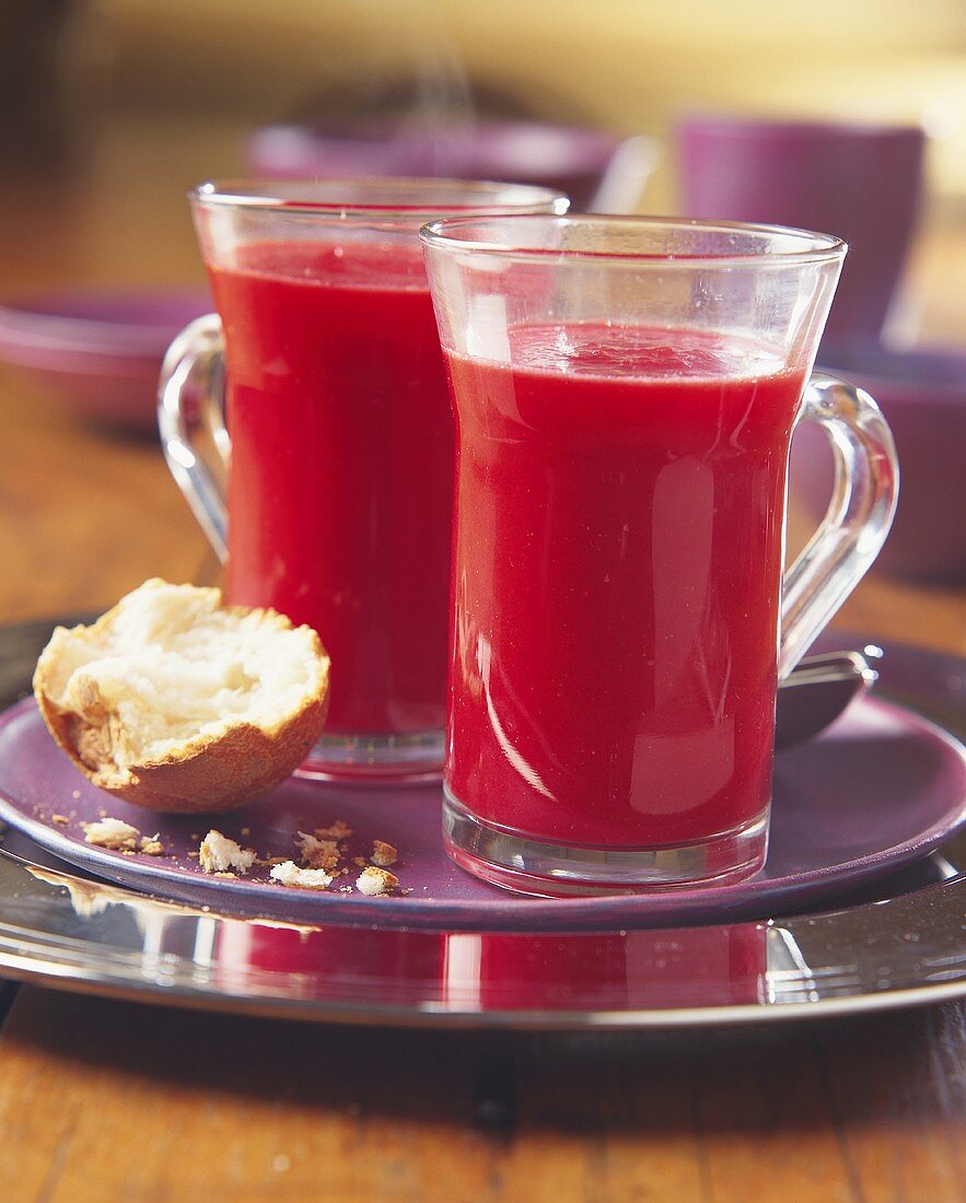 Strawberry soup in two glasses, half a bread roll beside them