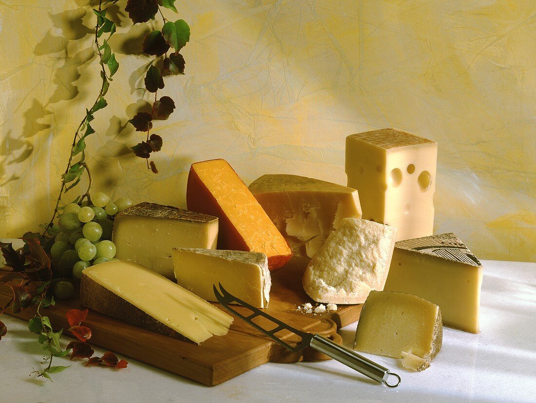 Various types of hard cheese on wooden board with grapes