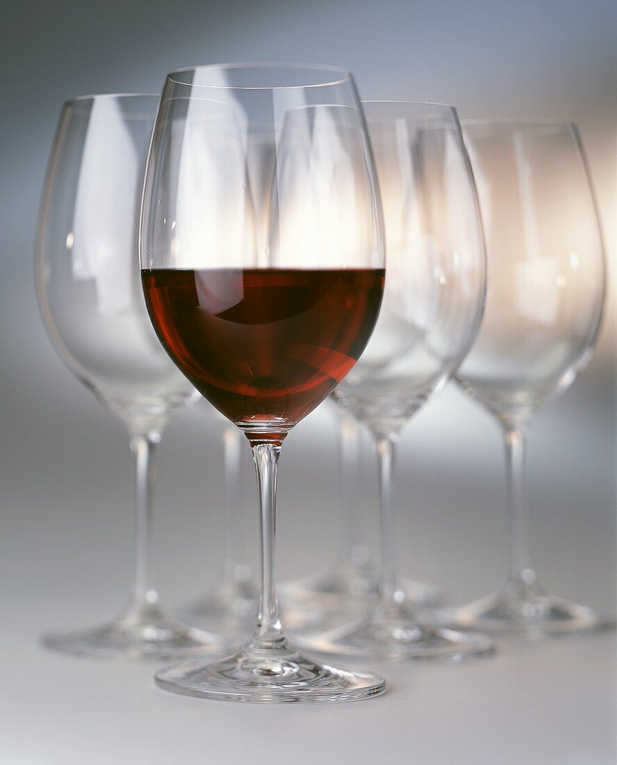 A half filled red wine glass in front of empty glasses