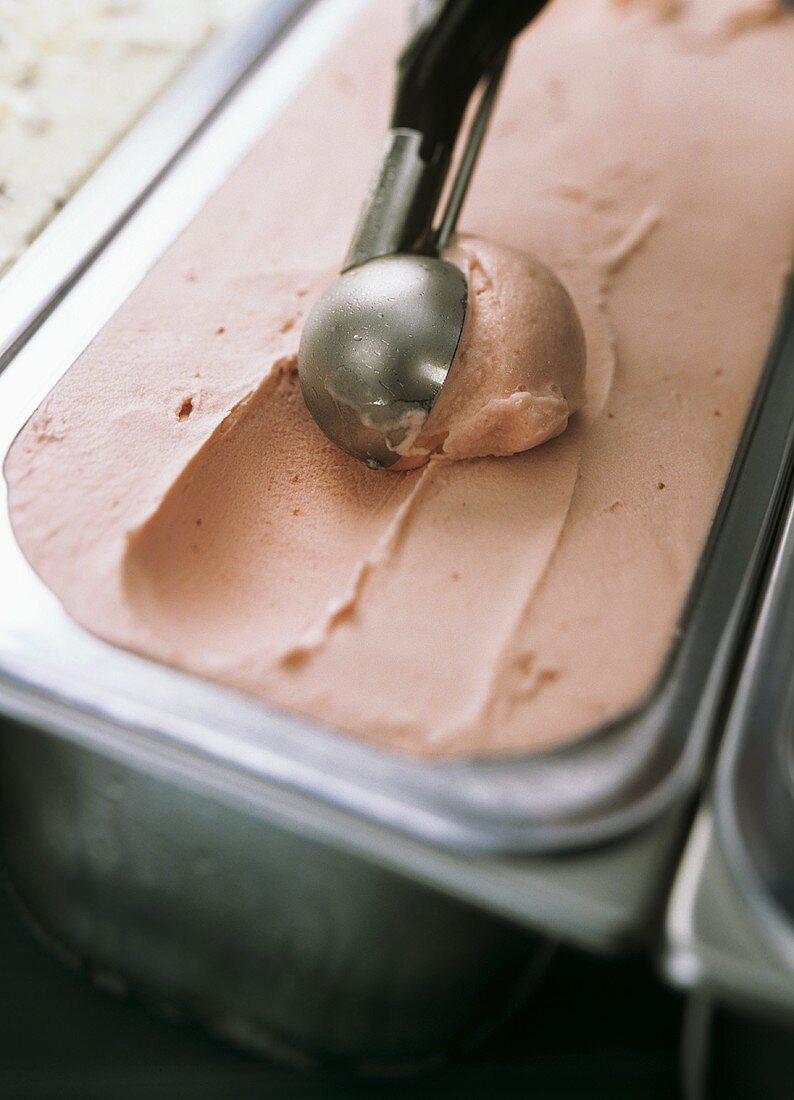 Strawberry ice cream in a container with scoop