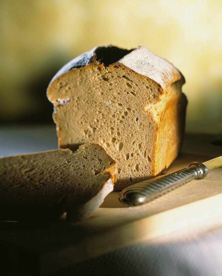 A tin loaf, cut into, on a wooden board with a knife