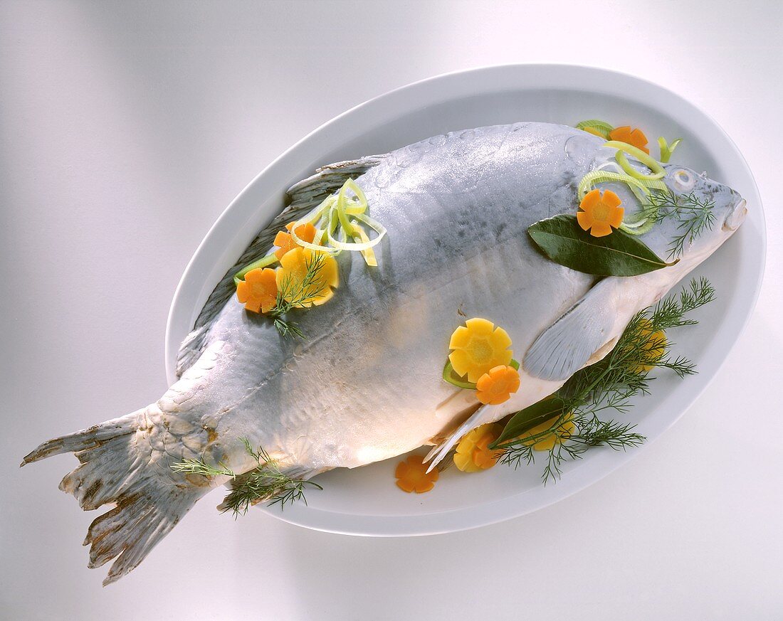 Carp cooked blue on a platter with vegetables and herbs