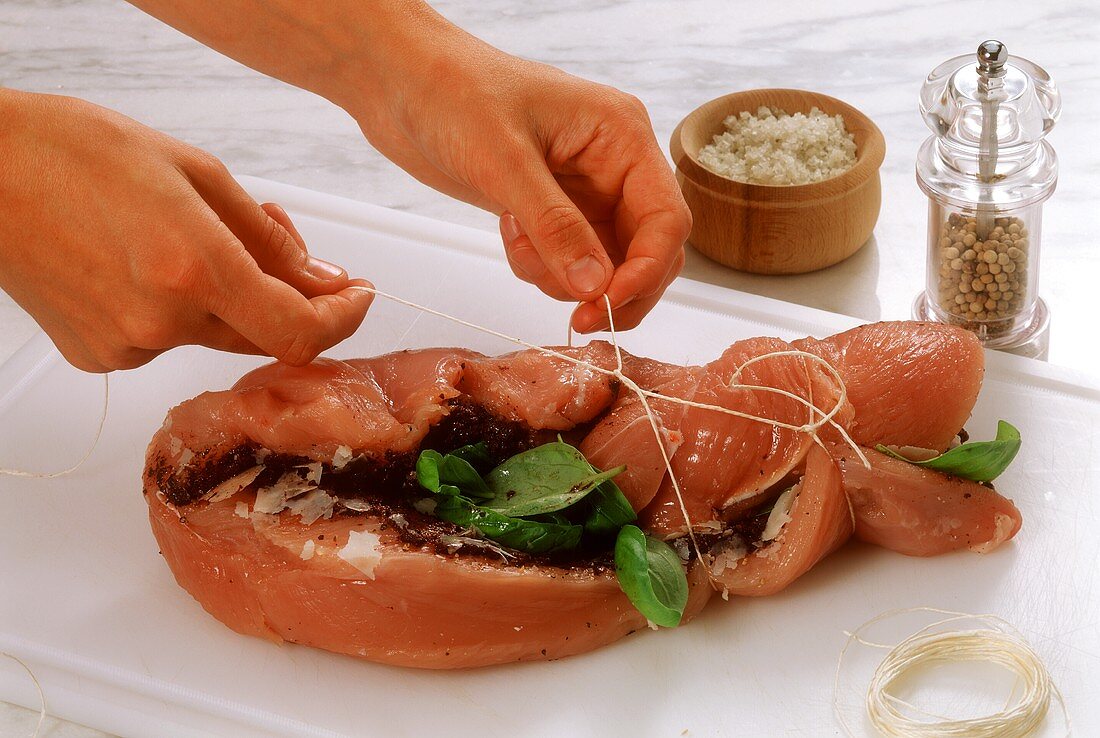 Tying up rolled roast with basil and olive paste