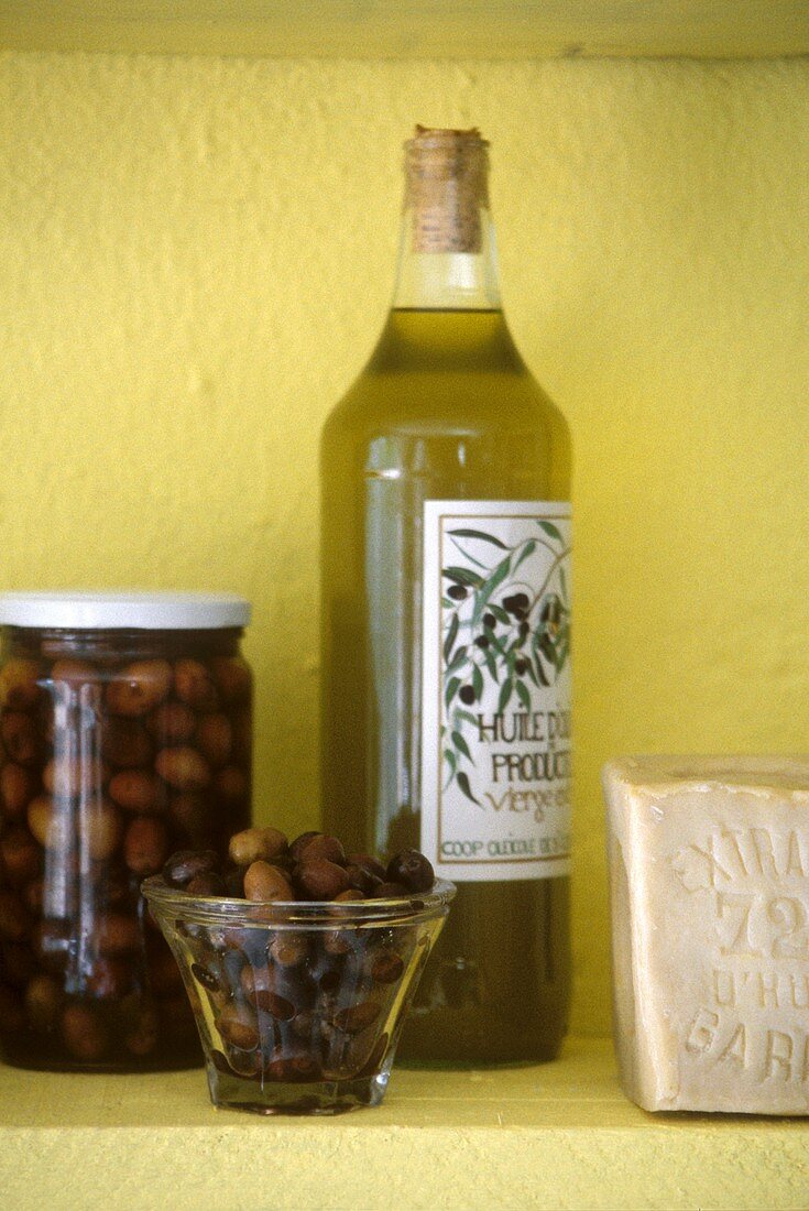 Olivenöl und schwarze Oliven vor gelber Wand