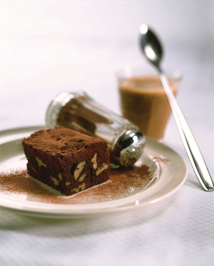 Brownie, mit Kakaopulver bestreut, auf Teller; Kaffee