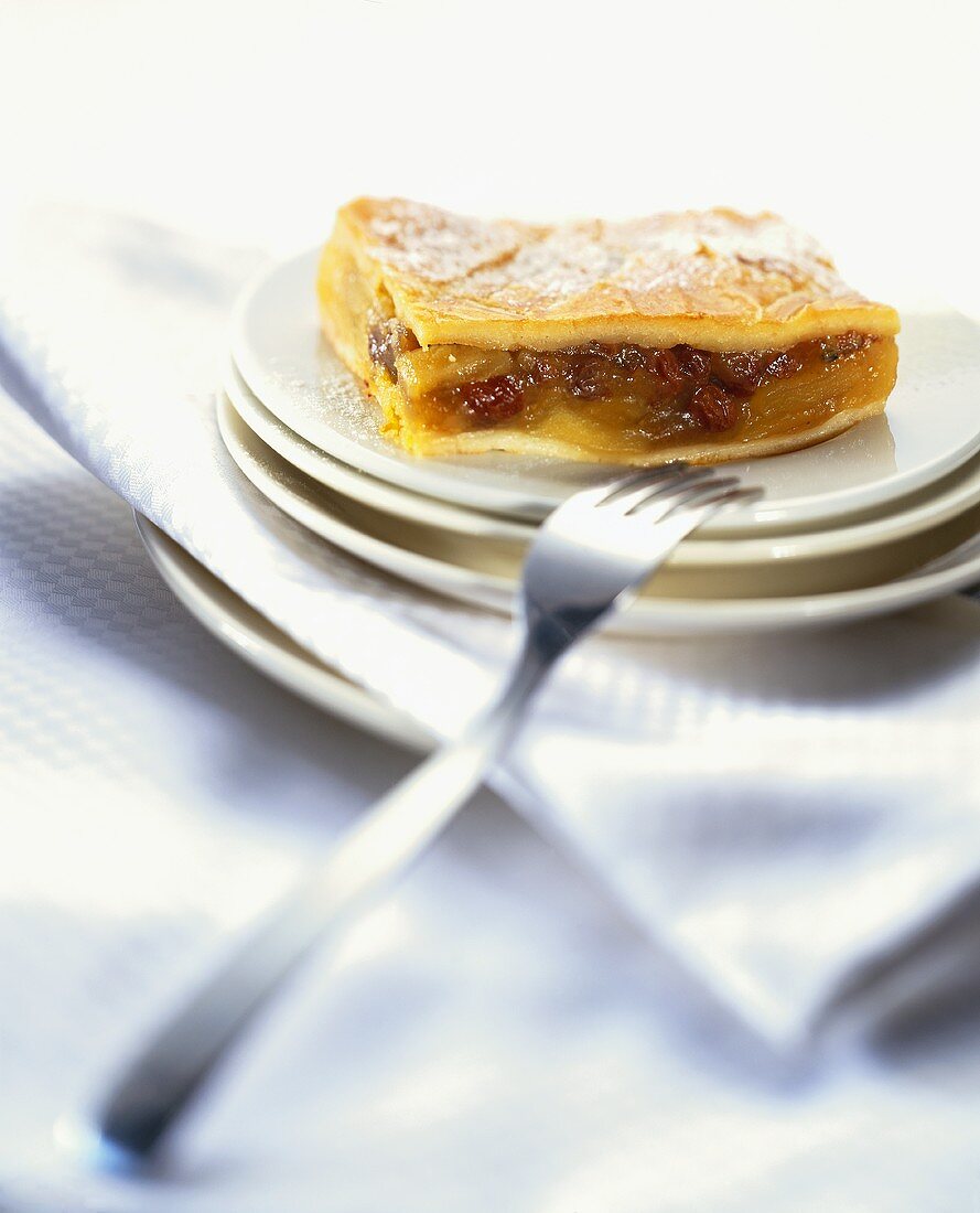 Ein Stück Apfelkuchen mit Rosinen auf Tellerstapel