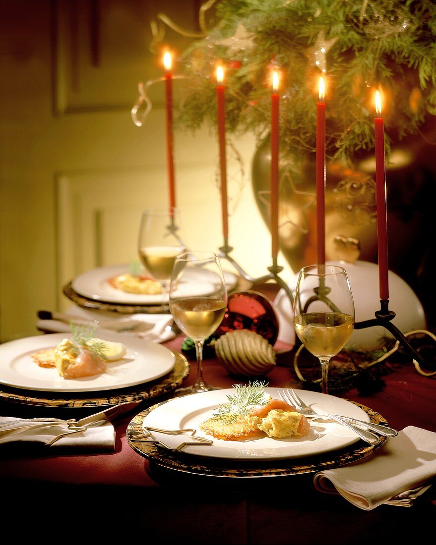Weihnachtlich gedeckter Tisch mit Lachsgericht und Weißwein