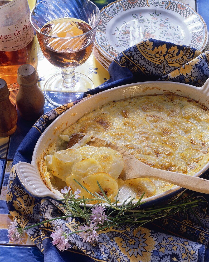 Potato gratin with wooden spoon in baking dish; rose wine