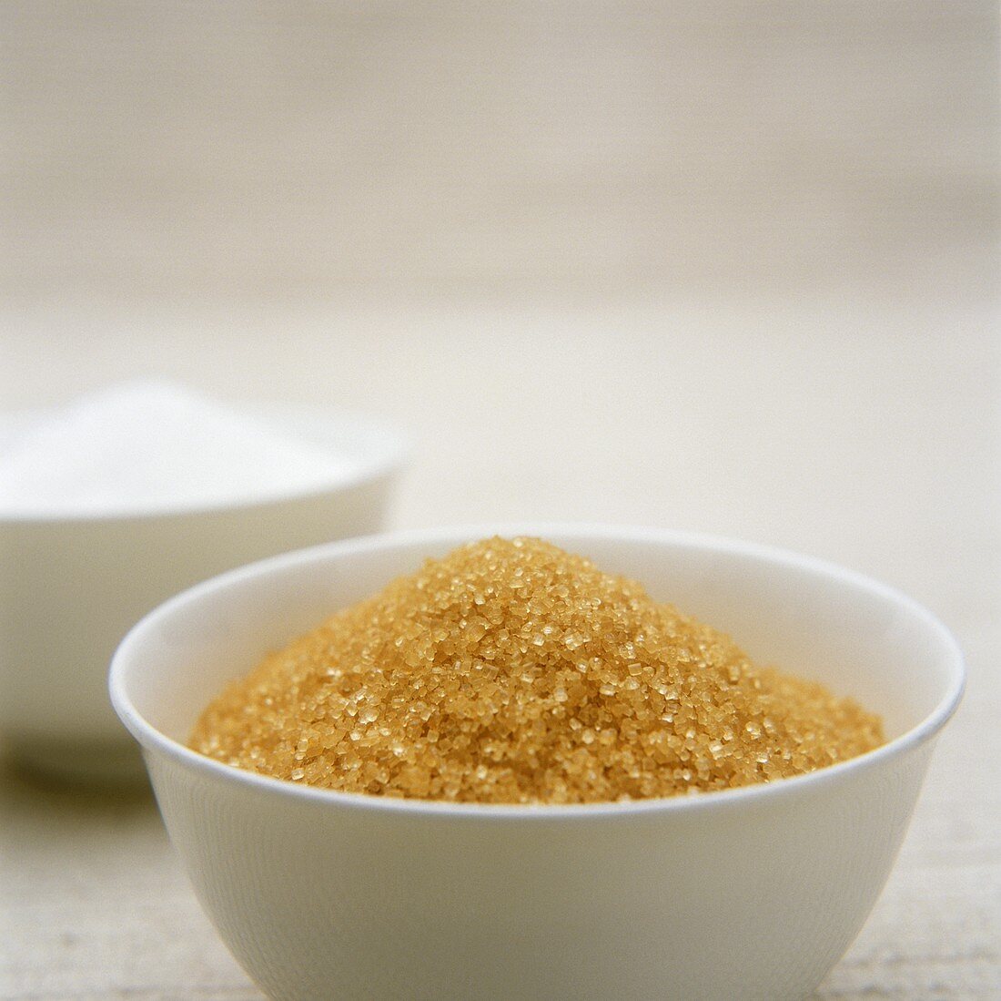 Brown sugar in white bowl in front of white sugar