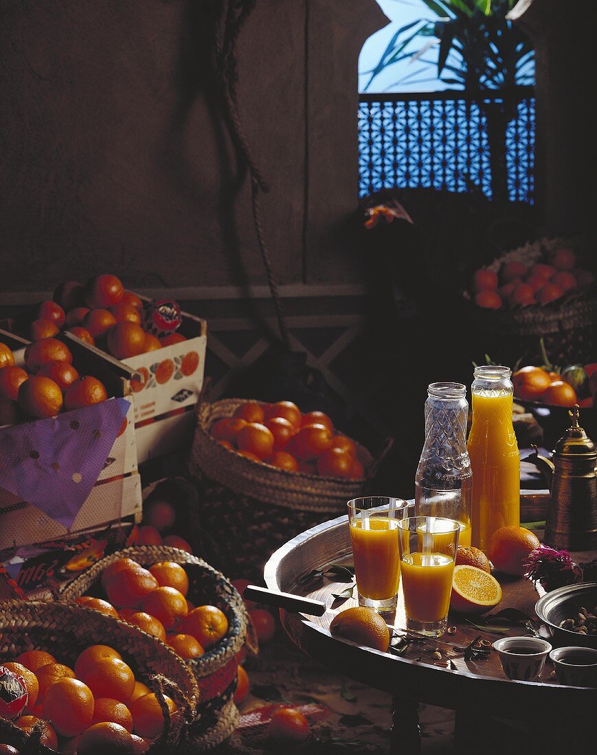 Orangensaft in Flaschen und Gläsern, umgeben von Orangen
