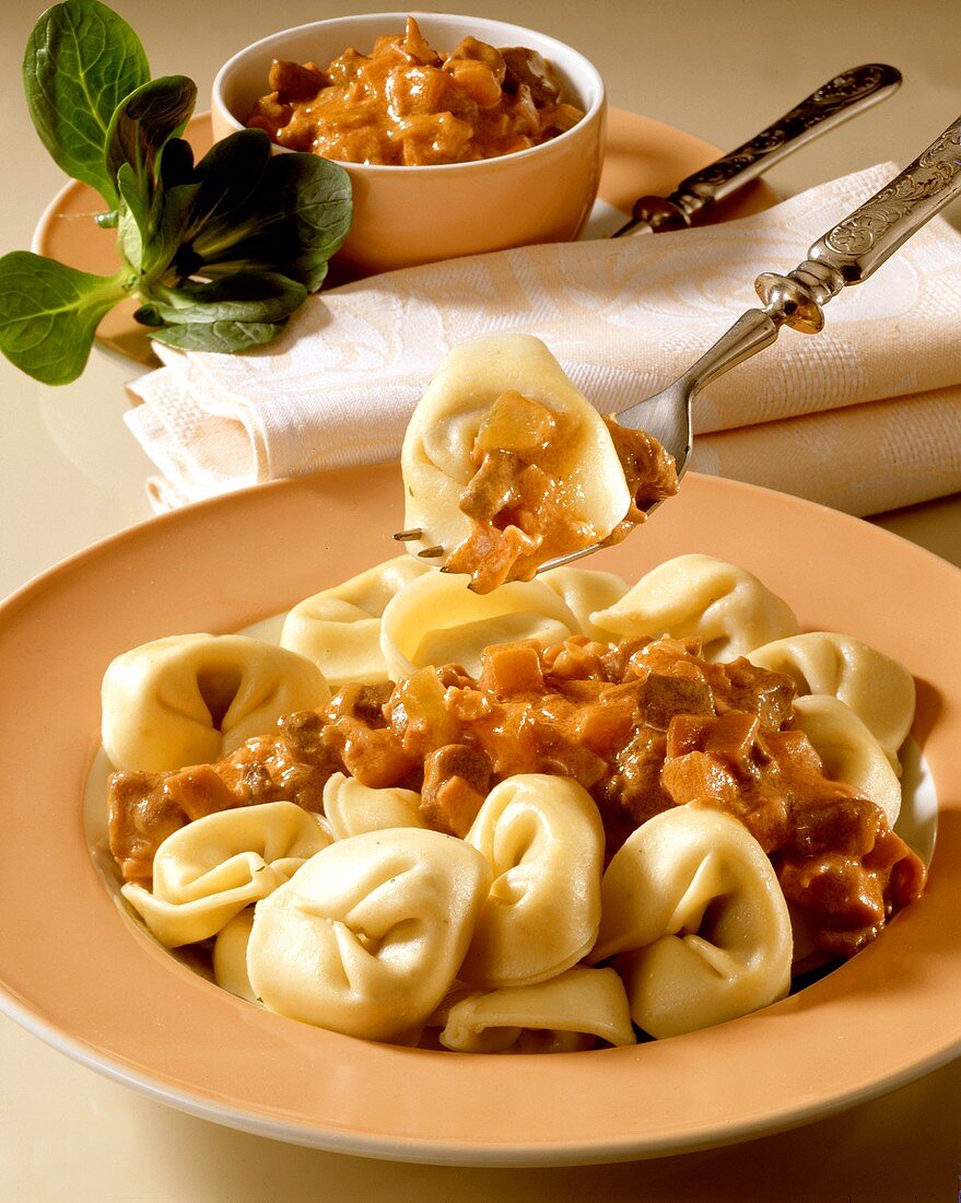 Tortellini mit Fleischsauce auf Teller und Gabel darüber