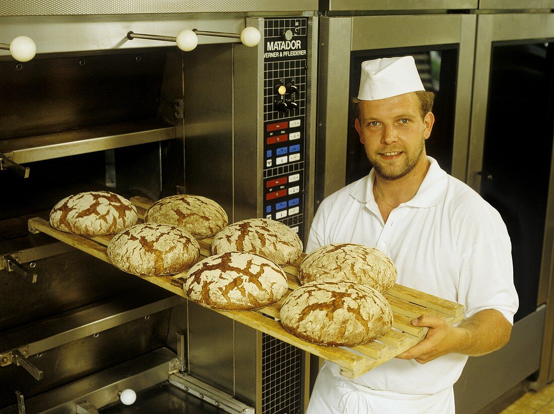 Baker with baked loaves at the oven