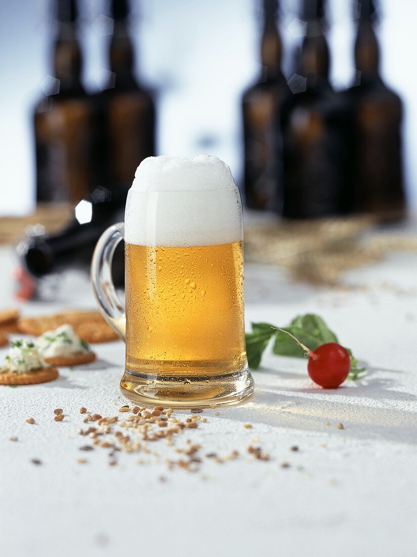 Cold beer in a glass tankard; Radish; Cracker; Beer bottles