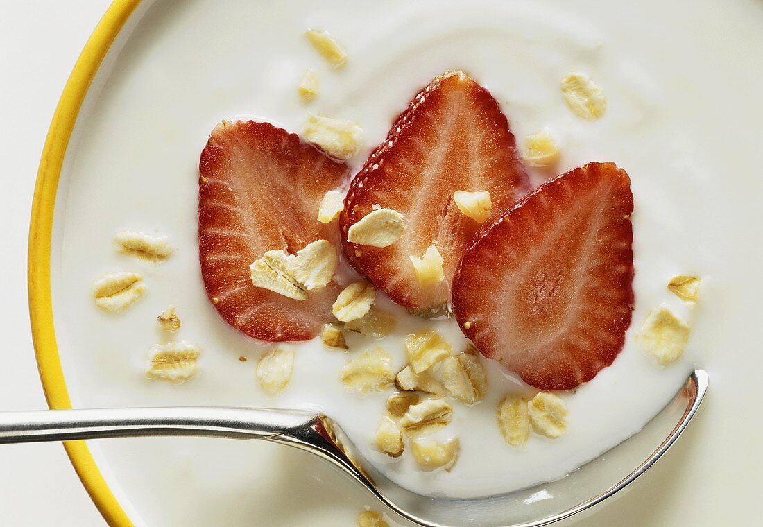 Yoghurt with strawberries and rolled oats in a bowl with spoon