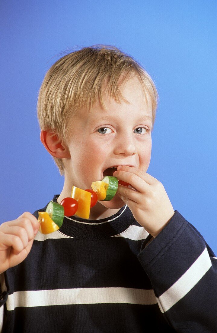Small boy biting into vegetable kebab