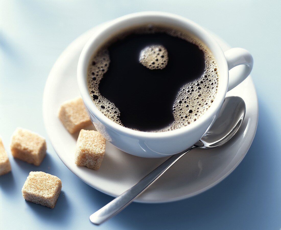 A cup of black coffee with raw sugar lumps