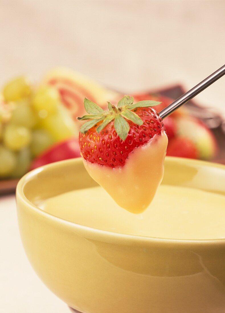 White chocolate fondue with strawberry on fondue fork