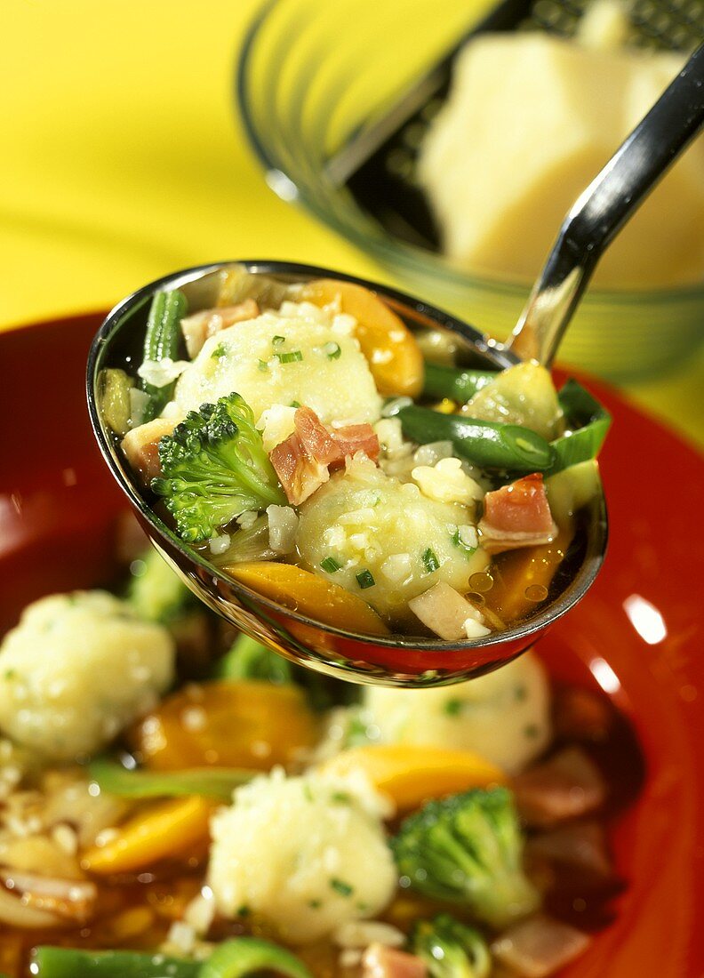 Gemüsesuppe mit Schnittlauchklösschen auf Kelle über Teller