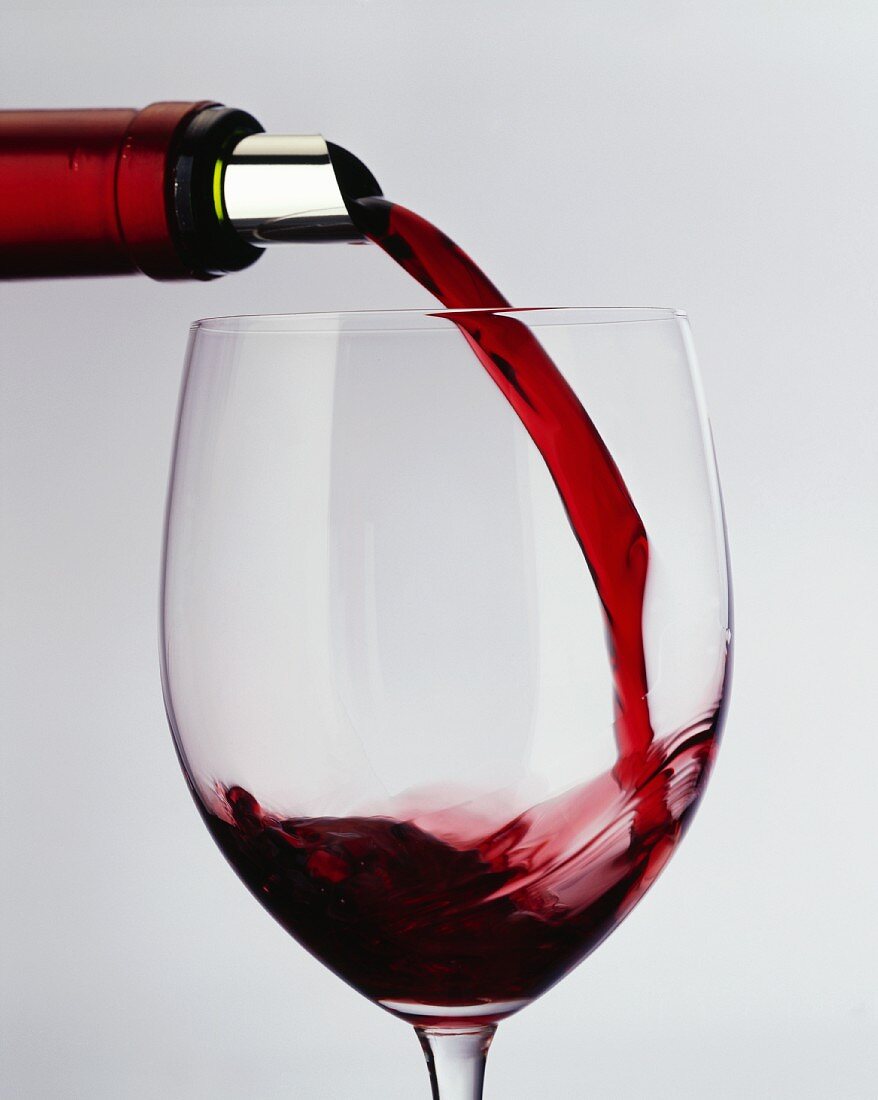 Pouring red wine from bottle with silver foil into a glass