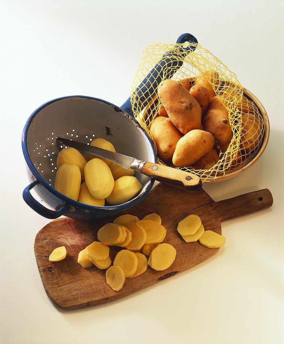 Potatoes in net and strainer and slices on chopping board