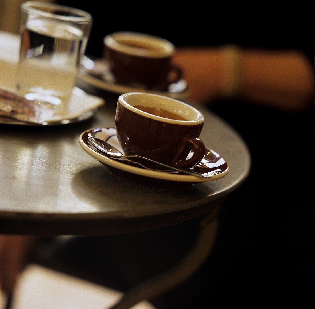 Two espresso cups and a glass of water on bistro table