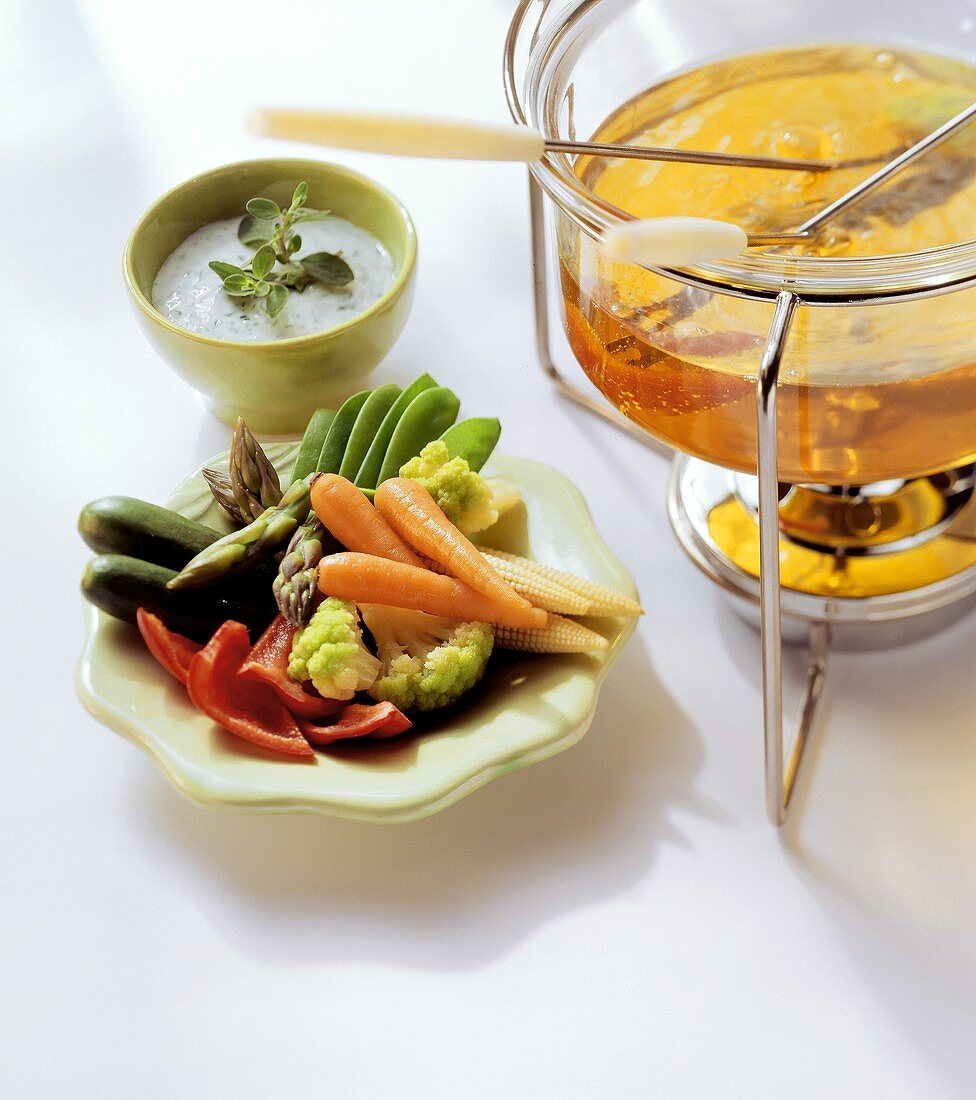 Fondue pot, raw vegetables on plate and herb dip