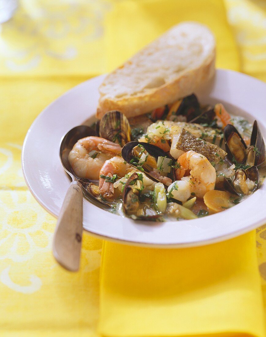 Fish soup with seafood on plate with bread and spoon