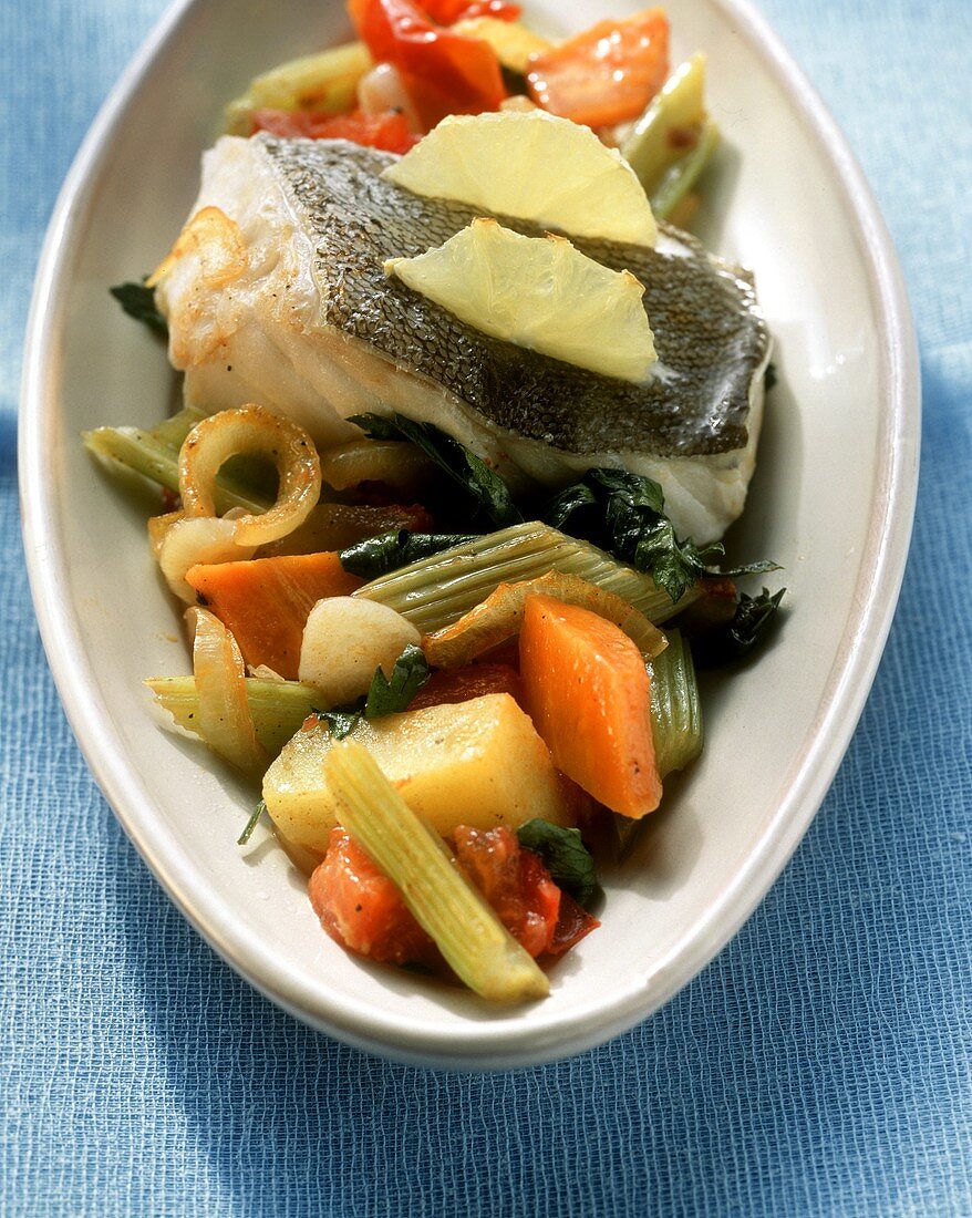 Oven-baked fish with lemon and vegetables on white plate