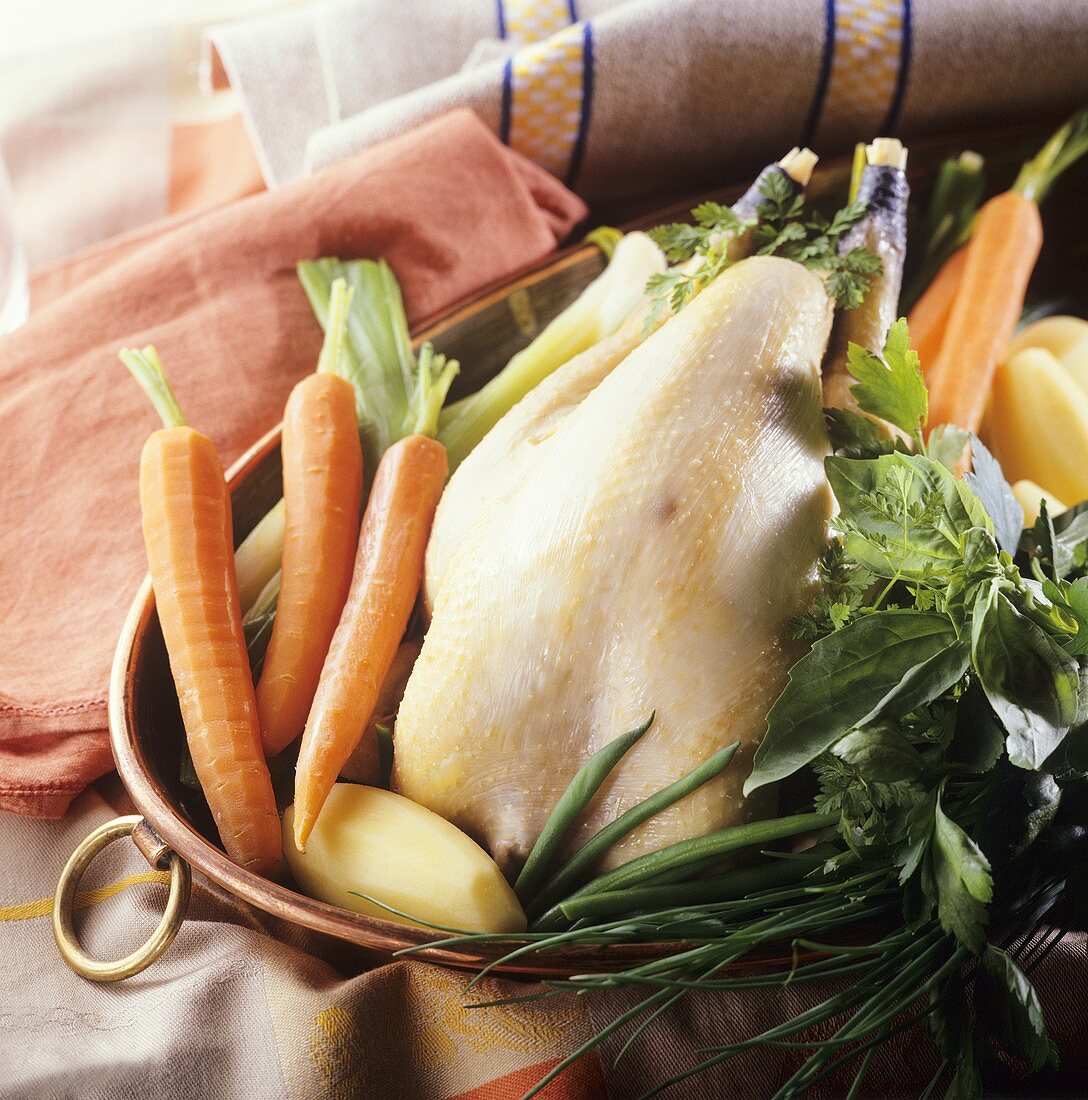 Suppenhuhn mit Gemüse und Kräutern im Topf