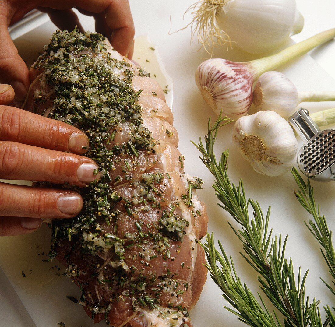 Rubbing rolled pork joint with herbs