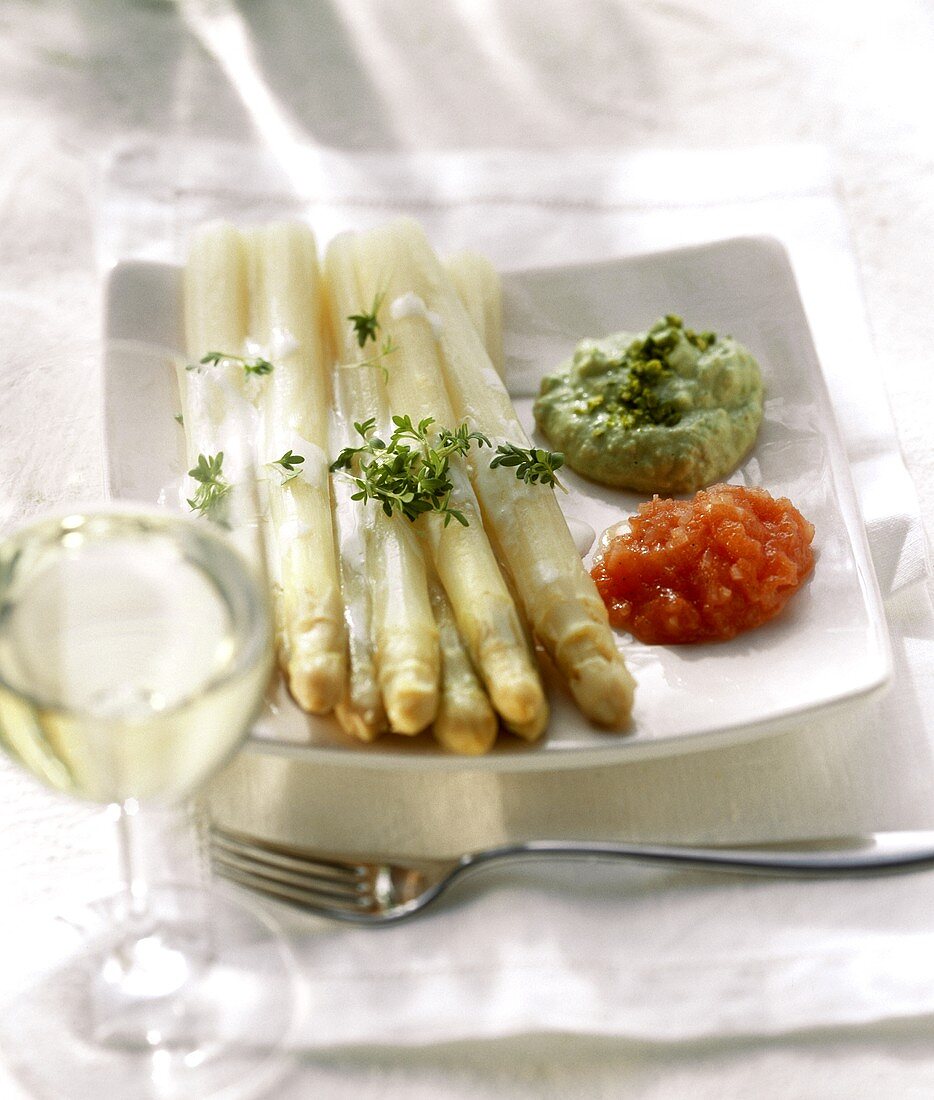 Weisser Spargel mit drei Saucen auf Teller; Weissweinglas