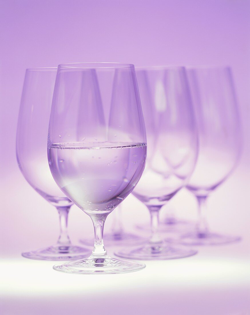 Mineral water in glass in front of a few empty glasses